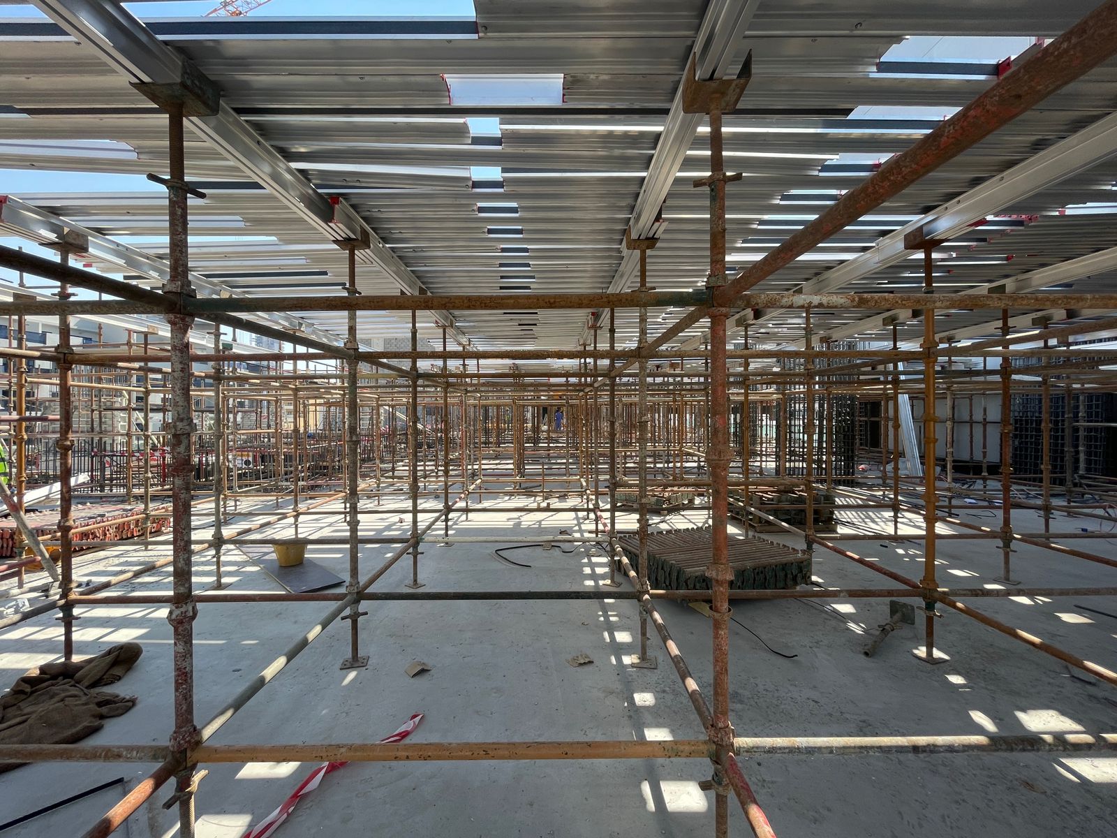 Pearl House By Imtiaz A construction site featuring metal scaffolding, a concrete floor, and natural light streaming through openings.